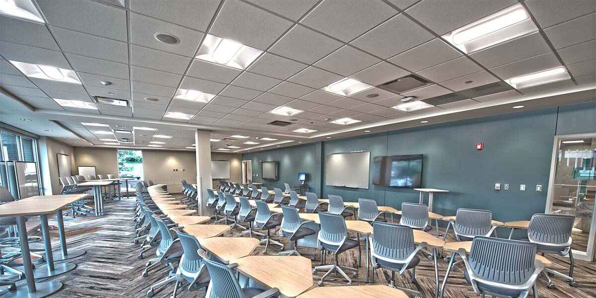 A modern classroom featuring multiple chairs with small study tables, a stylish ceiling design, and elegant lighting